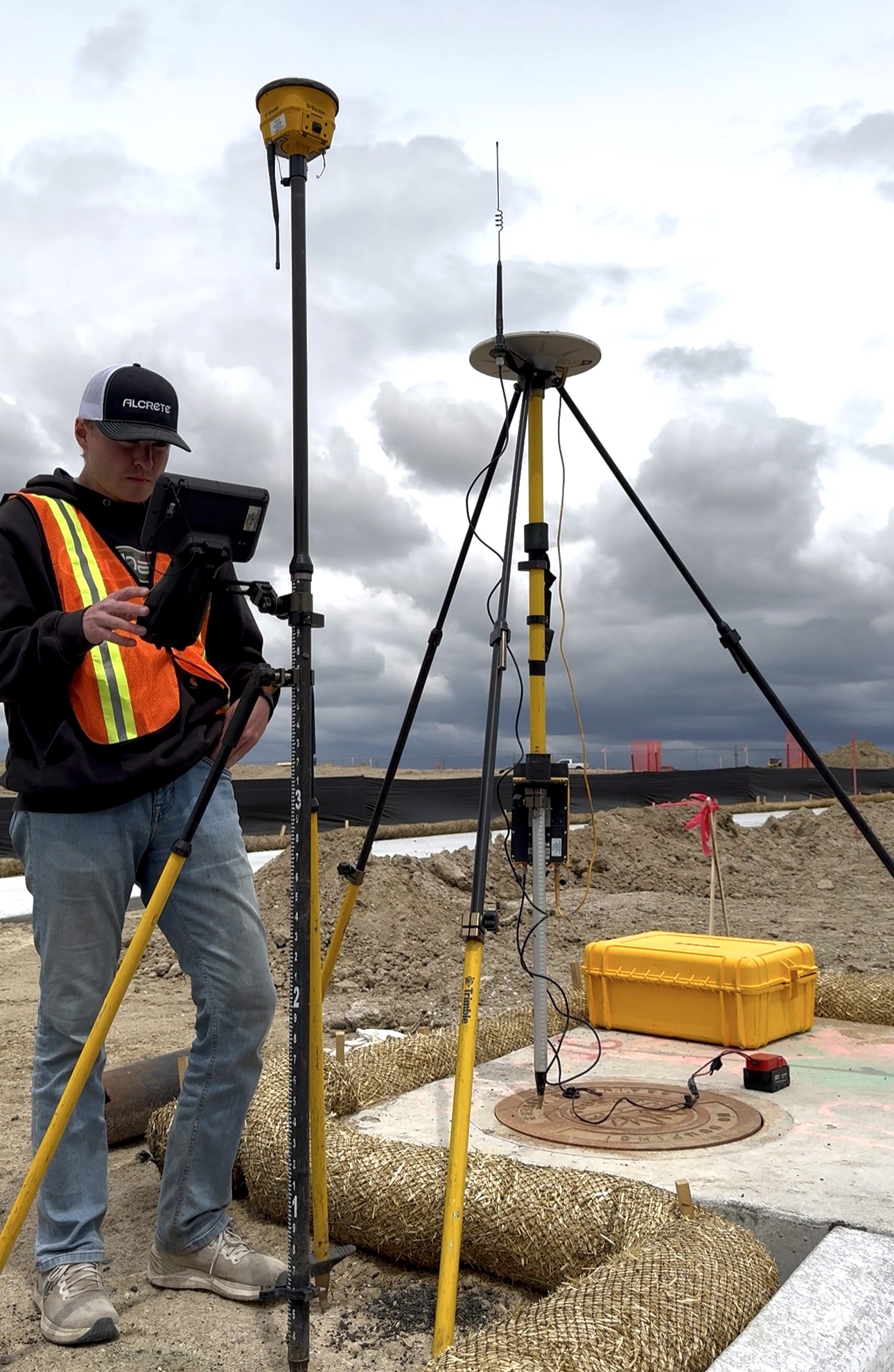 Sean standing with Trimble GPS equipment and controller under a stormy sky